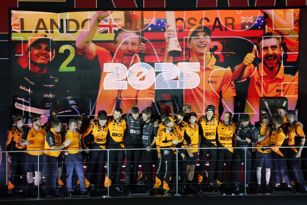 McLaren team in orange kit celebrating the 2025 constructors’ title on the podium gantry.