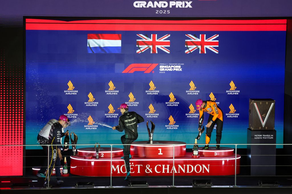 Singapore podium scene with Russell in the centre, Verstappen left and Norris right as champagne sprays.