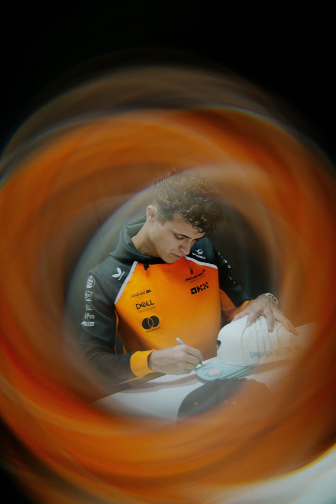 Lando Norris signs merchandise, photographed through an orange lens swirl ahead of the São Paulo weekend
