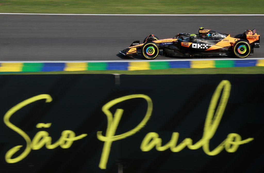 McLaren car at Interlagos during 2025 F1 Brazilian Grand Prix with São Paulo script on pit wall; yellow-green-blue kerbs visible.