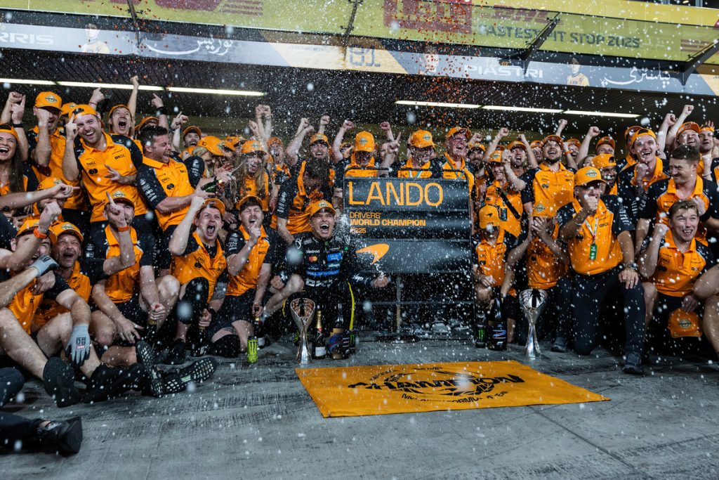 Lando Norris celebrates his world championship with McLaren team members in parc ferme amid champagne spray.